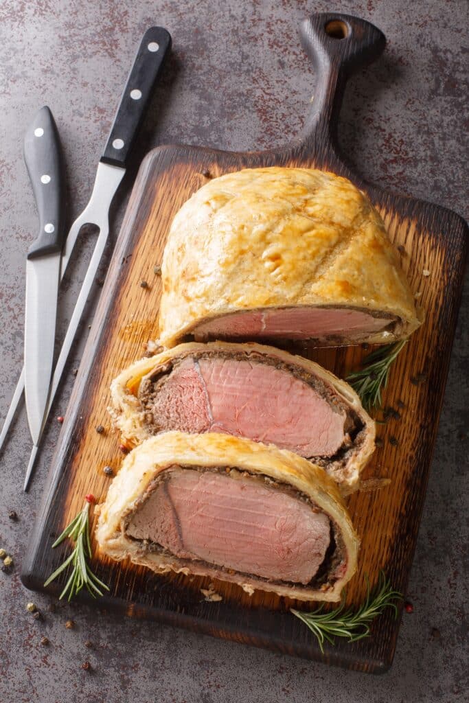 High angle beef wellington cooking or boeuf en crout cut into slices on a chopping board grey background Vertical top view from above | Aux Fourneaux Bœuf Wellington la vraie recette traditionnelle