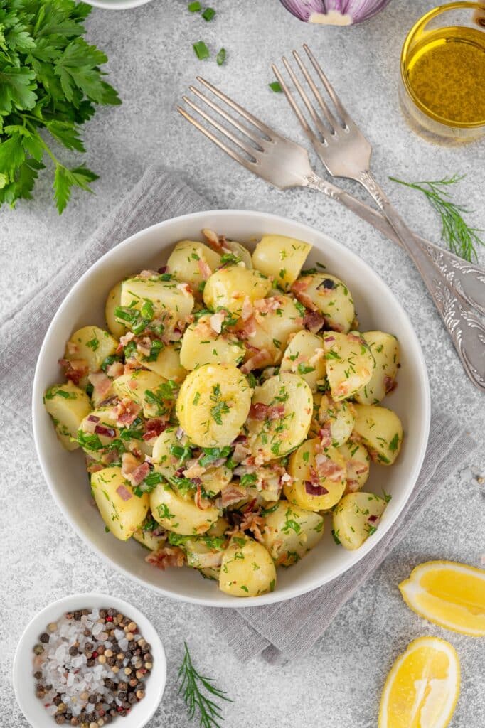 Warm potato salad with bacon onion fresh herbs and vinegar dressing in a bowl on a gray concrete background German Kartoffelsalat | Aux Fourneaux vraie salade de pommes de terre grand-mère traditionnelle