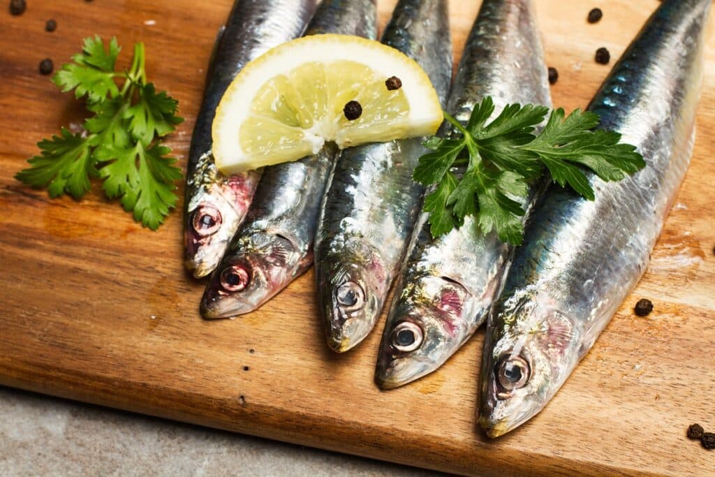 Sardinas crudas y naturales sobre una tabla de madera rústica con rodajas de limón y perejil Vista superior | Aux Fourneaux Comment préparer des sardines fraîches facilement