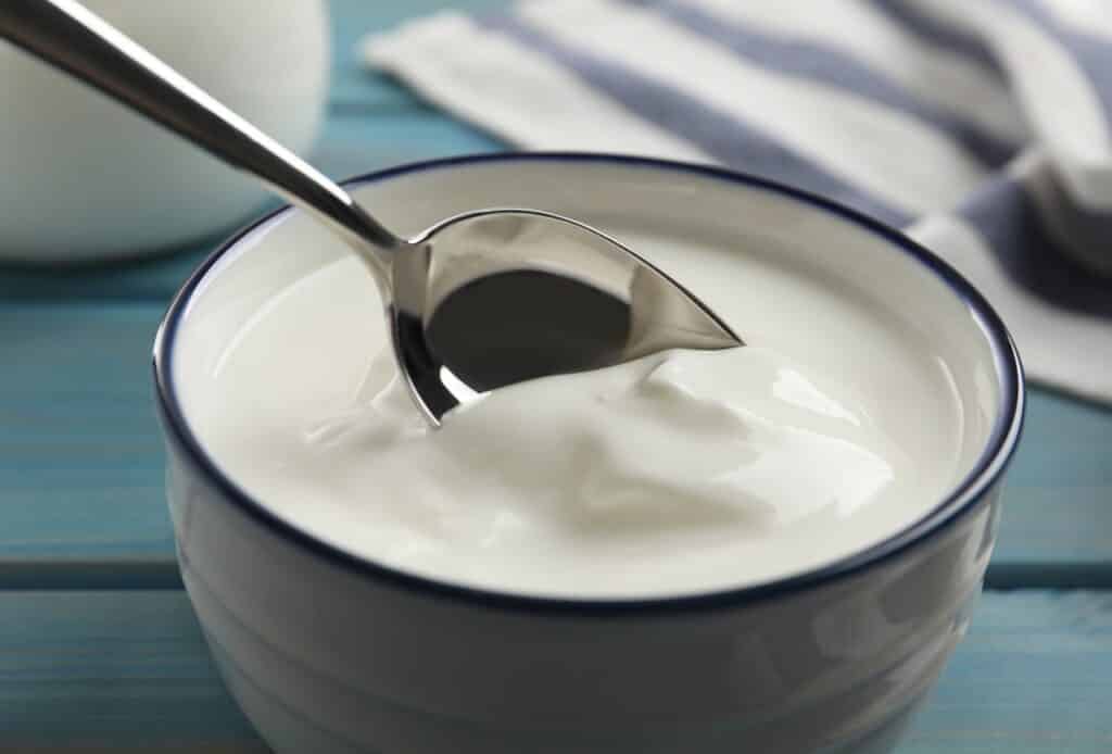 Eating tasty yogurt from bowl on light blue wooden table closeup | Aux Fourneaux Yaourt grec bienfaits valeurs nutritionnelles et conseils de consommation
